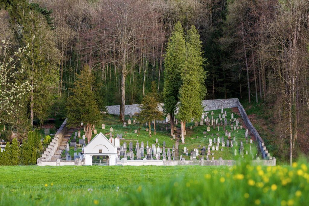 Friedhof mit Grabsteinen und einem weißen Gebäude im Wald, Österreich