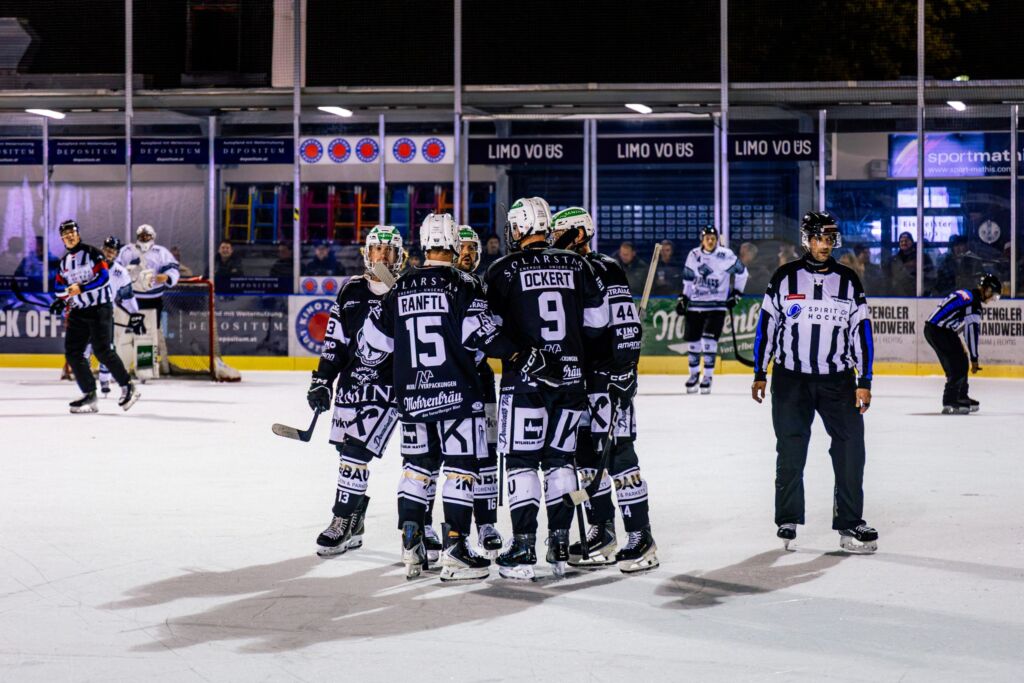 Eishockey-Spieler mit ihren Trainern auf dem Eis, Schiedsrichter im Hintergrund