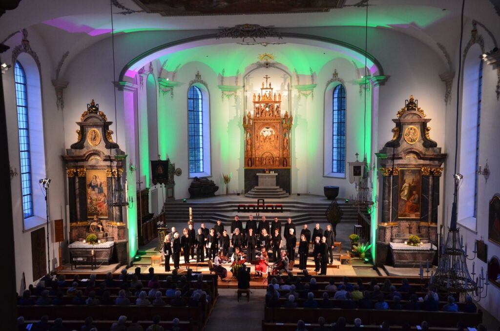 Chor und Musiker treten in der Kirche St. Michael in Wien auf, beleuchtet in Grün und Lila.